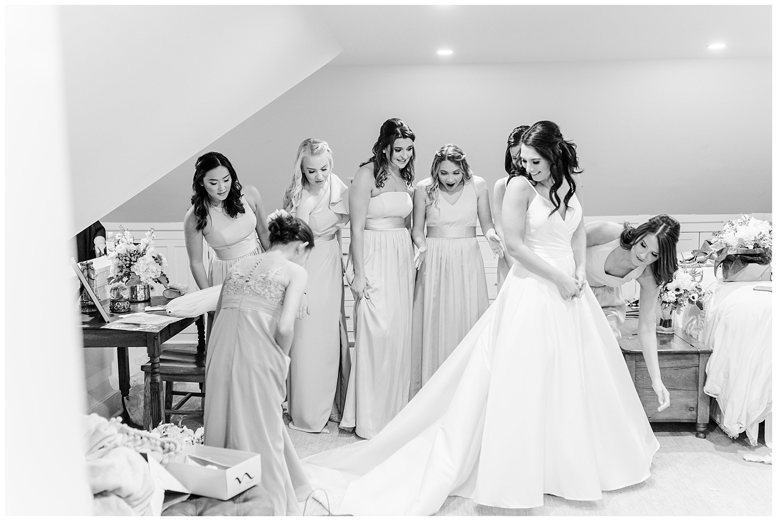 bridesmaids help bride button the back of her wedding dress with long train