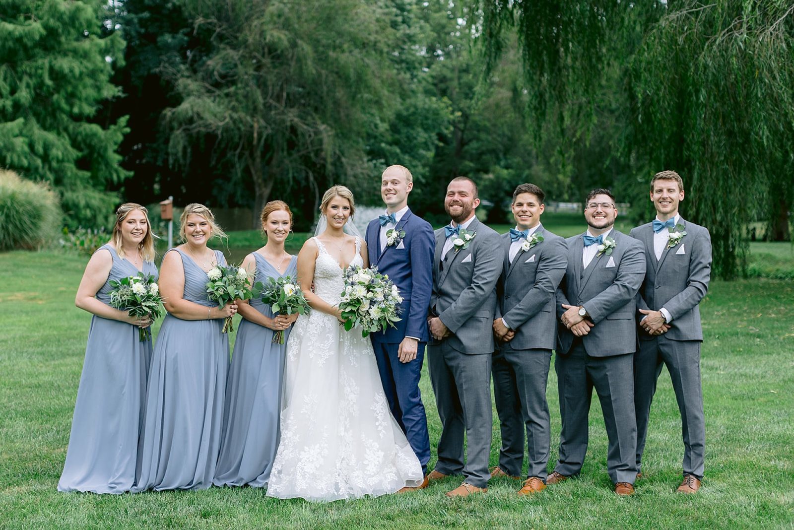 portraits of the full bridal party in blue full length gowns posing beneath the willow trees at historic acres of hershey